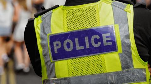 The back of a police officer's hi-viz vest with the word police in white capital letters on a blue rectangle background.