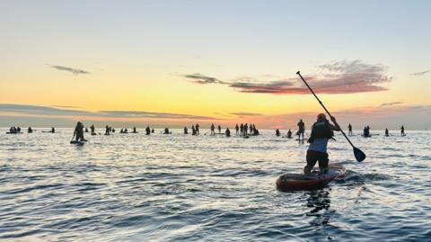 A large number of paddleboarders on the water as the sun rises.