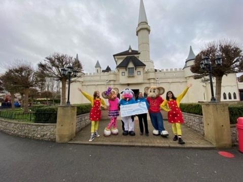 White castle in background with theme park characters in foreground holding a large cheque