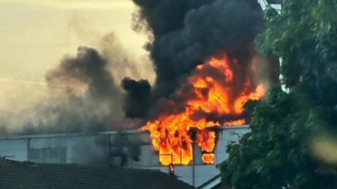 Black smoke above flames and the top of a building. 