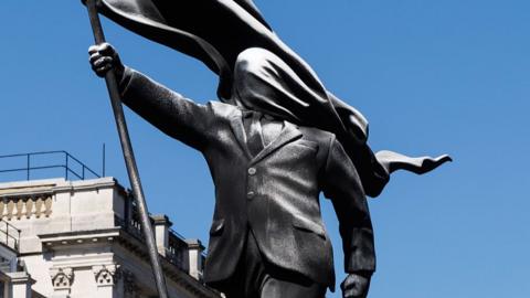 Close up of the statue showing a man holding a flag which is covering his face