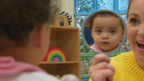 Baby playing with mirror, baby looks surprised at own reflection.