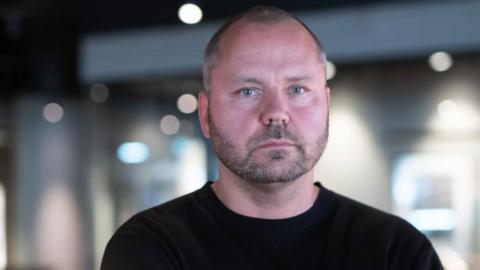 (Photo: Ola Sars, seen from the shoulders up, wears a black jumper and has short shaved brown hair going grey at the sides, blue eyes and stubble growth. He looks at the camera with a neutral expression. Credit: Rickard Croy)