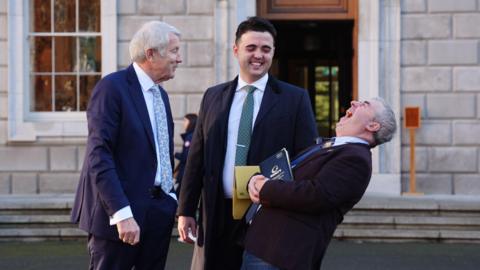 Members of Regional Independent Group (left to right) Michael Lowry, Barry Heneghan and Kevin "Boxer" Moran at Leinster House in Dublin. All are wearing suits, Kevin "Boxer" Moran is bent over laughing, with the others smiling at him.