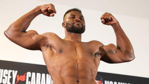 Francis Ngannou flexes and smiles while weighing in