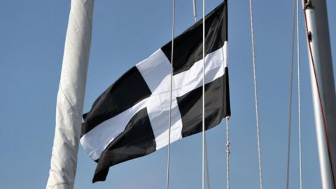 A Cornish flag, which is black with a white cross. It appears to be attached to a sail.