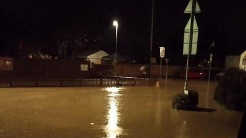 Flooded village roads captured on a phone camera late at night, with brown water where pavements and carriageways should be seen