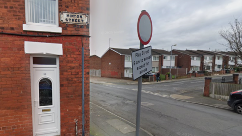 View of the corner of a row of terraced brick houses, with a road sign reading 'Hinton Street' attached to the wall.