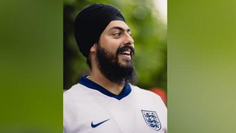 Jag Singh smiling, wearing a black turban and England shirt.