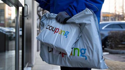 A Coupang employee holds packages in front of an apartment building in Bucheon, South Korea