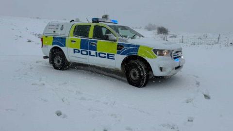 A 4x4 police car parked in snowy fields with blue lights on