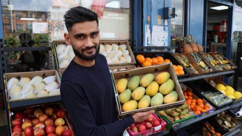 Shivam Pabari holding a box of mangos outside his fruit shop.