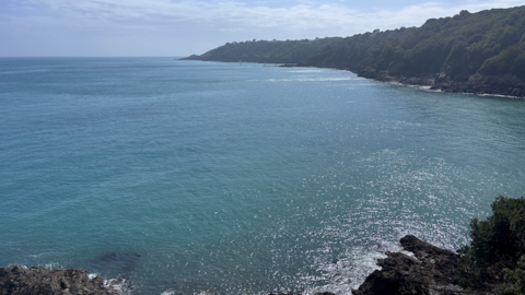 Cliffs in the distance and foreground with the ocean surrounding, blue skies and a few grey clouds in the distance.