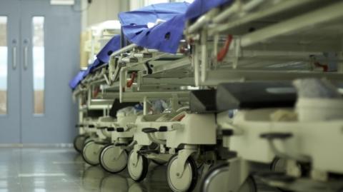 A stock image of a hospital corridor with gurneys and bed trolleys
