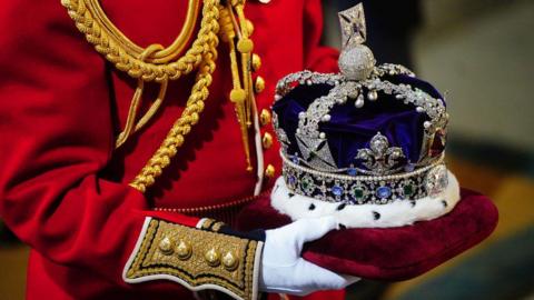 The Imperial State Crown is carried on a red velvet cushion by a liveried footman ahead of the State Opening of Parliament in the House of Lords in November 2023