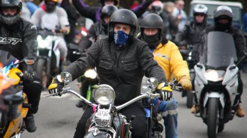 A convoy of motorbikes leaving the Woodhorn Museum in Ashington. They are all wearing leather jackets and helmets.