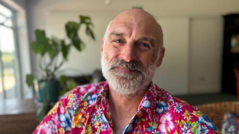 A bald man with a grey beard, wearing a brightly coloured shirt