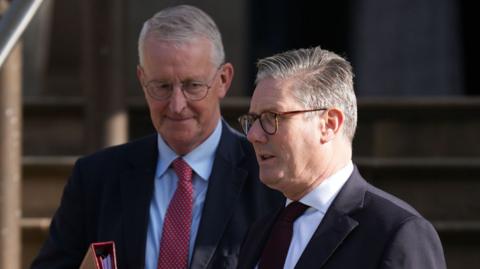 Northern Ireland Secretary Hilary Benn and Prime Minister Sir Keir Starmer stand next to each other. Both are middle-aged with grey hair wearing glasses.