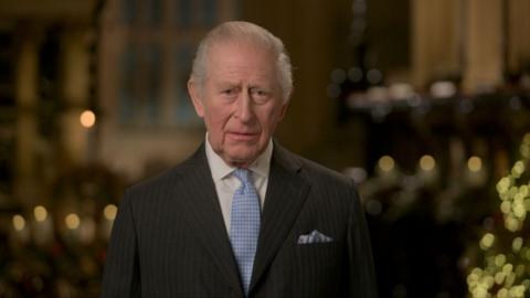 King Charles wearing a black suit and blue tie.