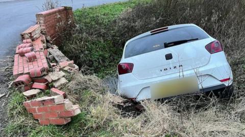 A white Seat Ibiza in a brook. The bridge's brick wall next to it is damaged.