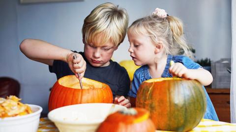 Two children carving pumpkins together.