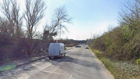A van drives down a tree- and bus-lined road