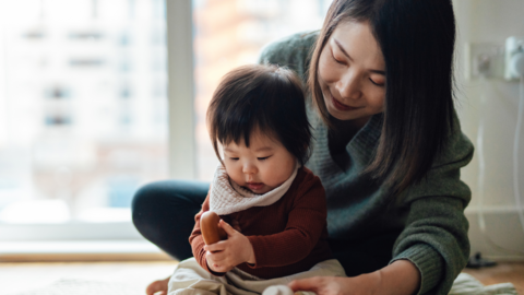 A mother with her child who is playing on the floor.