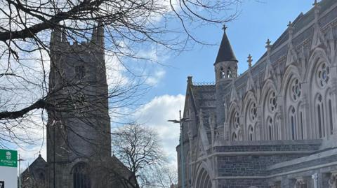 The outside of the Guildhall on the Royal Parade, Plymouth. There is a church to the left of the building which is grey and has 