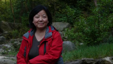 Chinese writer Fang Fang poses in red coat outside.