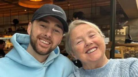 Charlie Quirke in baseball cap with his smiling mum Pauline Quirke looking to camera outdoors