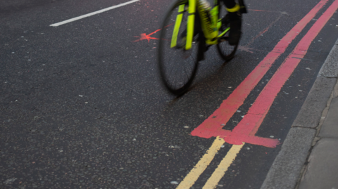 Double yellow lines by the side of the road, becoming double red lines towards the top of the picture