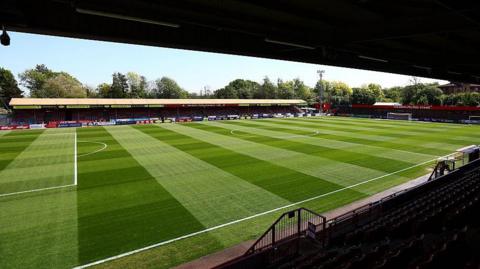 An empty photo of Crawley Town's Broadfield stadium from the main stand, in sunlight.