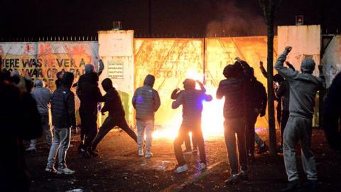 Young people, most with their hoods up, standing in front of an exploding petrol bomb in west Belfast