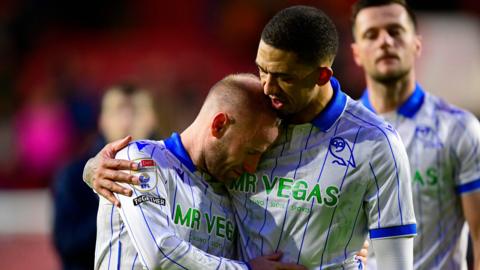Former Sheffield Wednesday captain Barry Bannan, wearing the club's away shirt of white with royal blue collar and vertical pinstripes, is comforted by team-mate Liam Palmer after a game