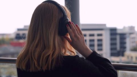 A woman with headphones on looking out of a window, turned away from the camera