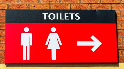 A large red sign with white lettering which reads Toilets, with a picture of a man and a woman below it