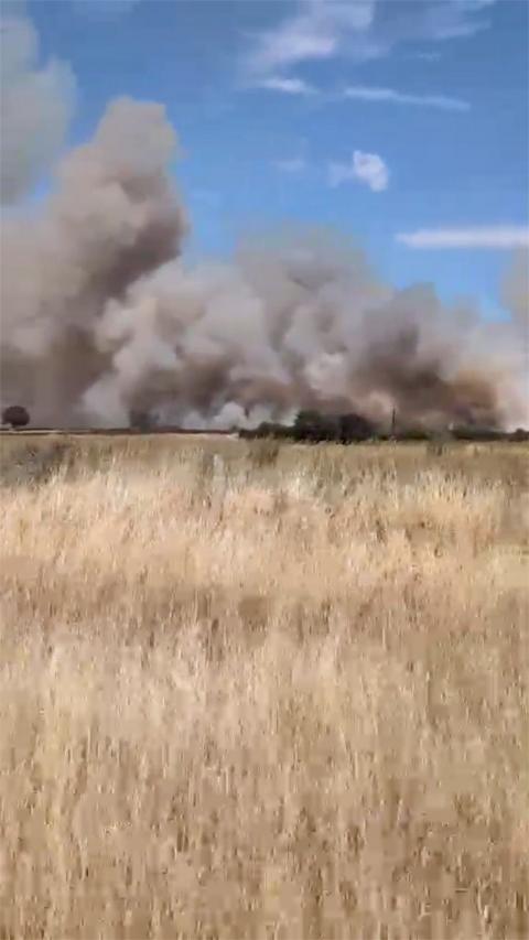 Smoke is rising from a field with hay into the blue sky.