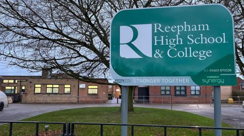 External photograph of the Reepham High School and College building, with a sign bearing the school's name in the foreground.