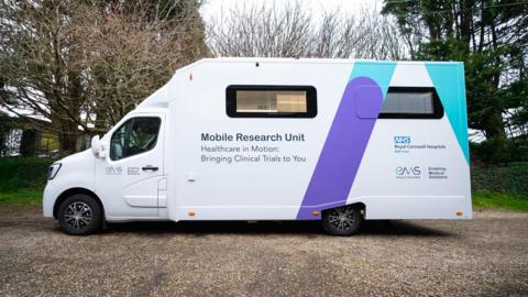 A white van with a purple and turquoise slash across the back and the words Mobile Research Unit written on the side.