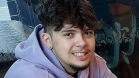 Cameron Arneaud looking at the camera smiling, wearing a lilac hoodie