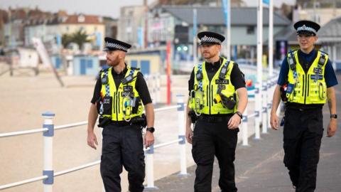 Three uniform officers on patrol along a beach front.
