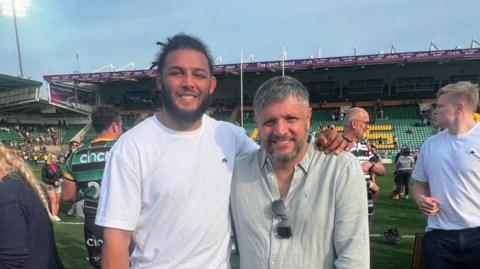 Arron with light-coloured hair and beard standing next to Lewis with dark hair and beard at a rugby stadium