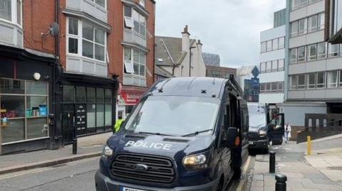 A large, black police van is parked in the road.