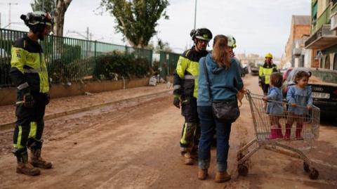 Firefighters talk with a woman transporting children in a shopping trolley in Sedavi, Valencia