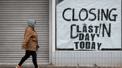 A person walks past a closed down shop which says "Closing down. Last day today" in the window.  