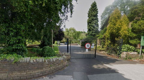 Gates at the entrance to a park, with a 5mph sign and trees in the background