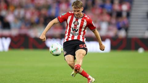 Harrison Jones puts his left foot through the ball wearing Sunderland home kit red and white stripes
