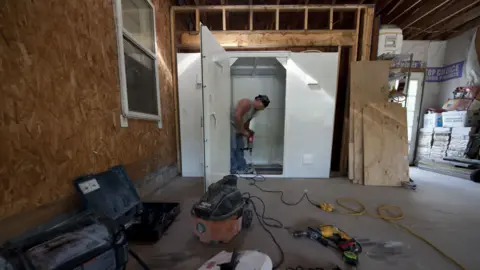 A man holds a piece of equipment while building a tornado shelter