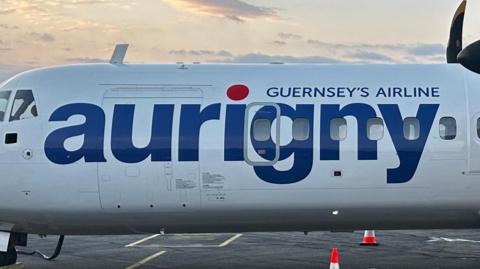 A picture of the side of a Aurigny plane. There is a white plan which reads in blue text - "Guernsey's Airline aurigny'
