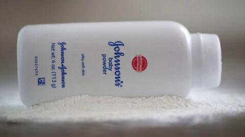 A bottle of Johnson and Johnson Baby Powder is seen in a photo illustration placed on its side on top of some white baby powder
